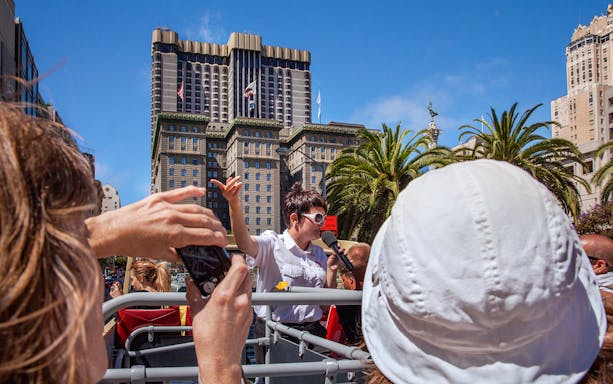 Tour guide speaking on a Big Bus in San Francisco with city buildings in the background.
