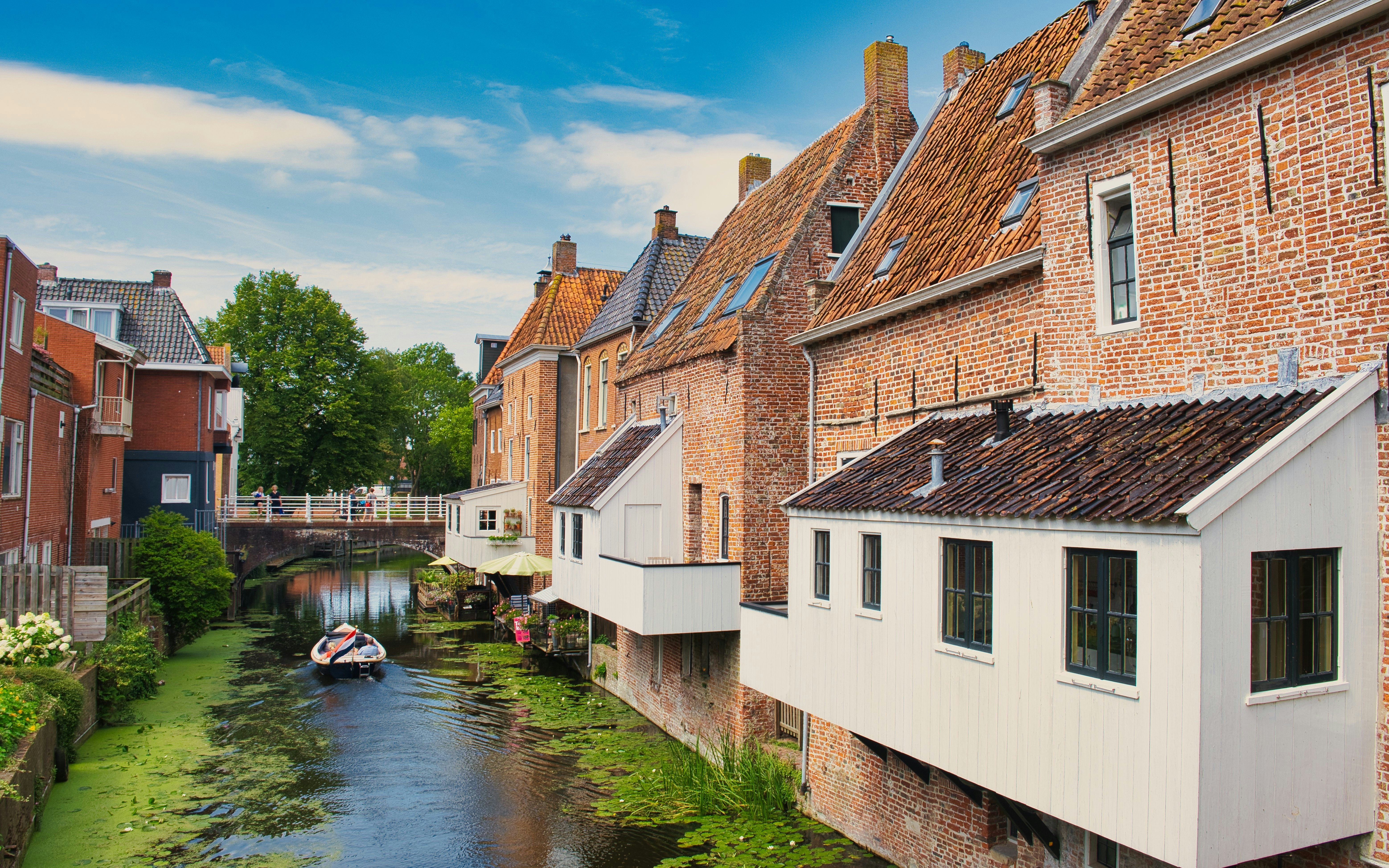 Groningen canal with boat and historic brick buildings near a bridge.