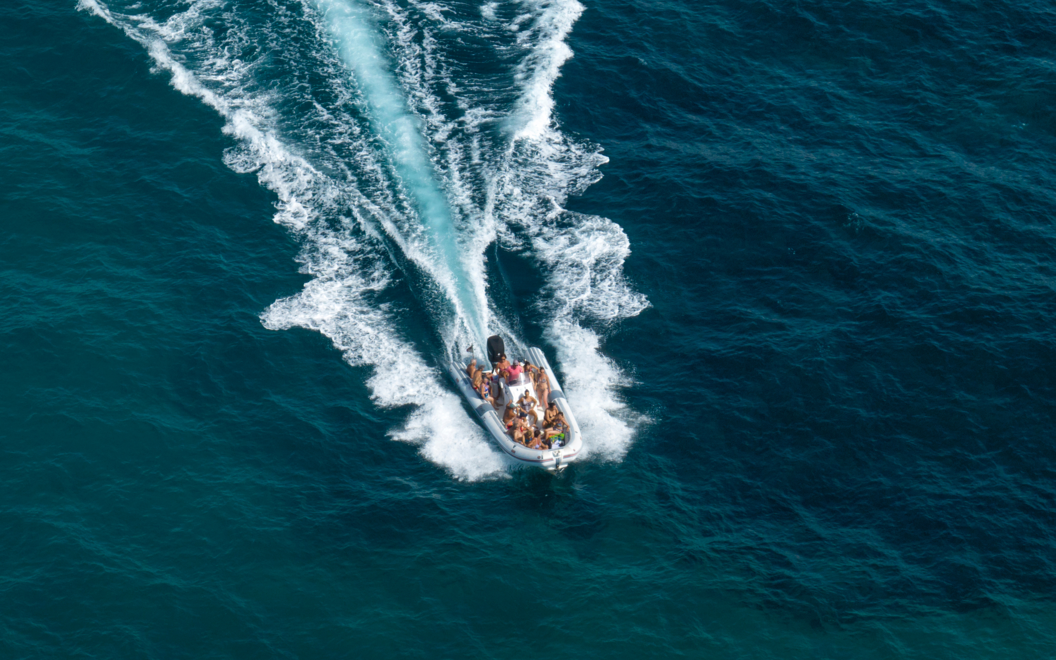 Aerial view of a dinghy with passengers speeding through blue ocean waters.