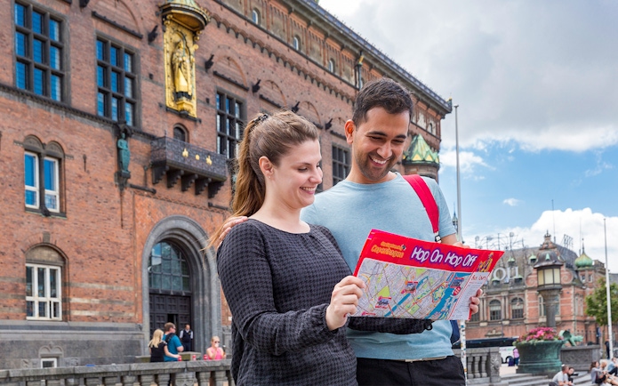 Friends examining Copenhagen HOHO bus route map near historic building.