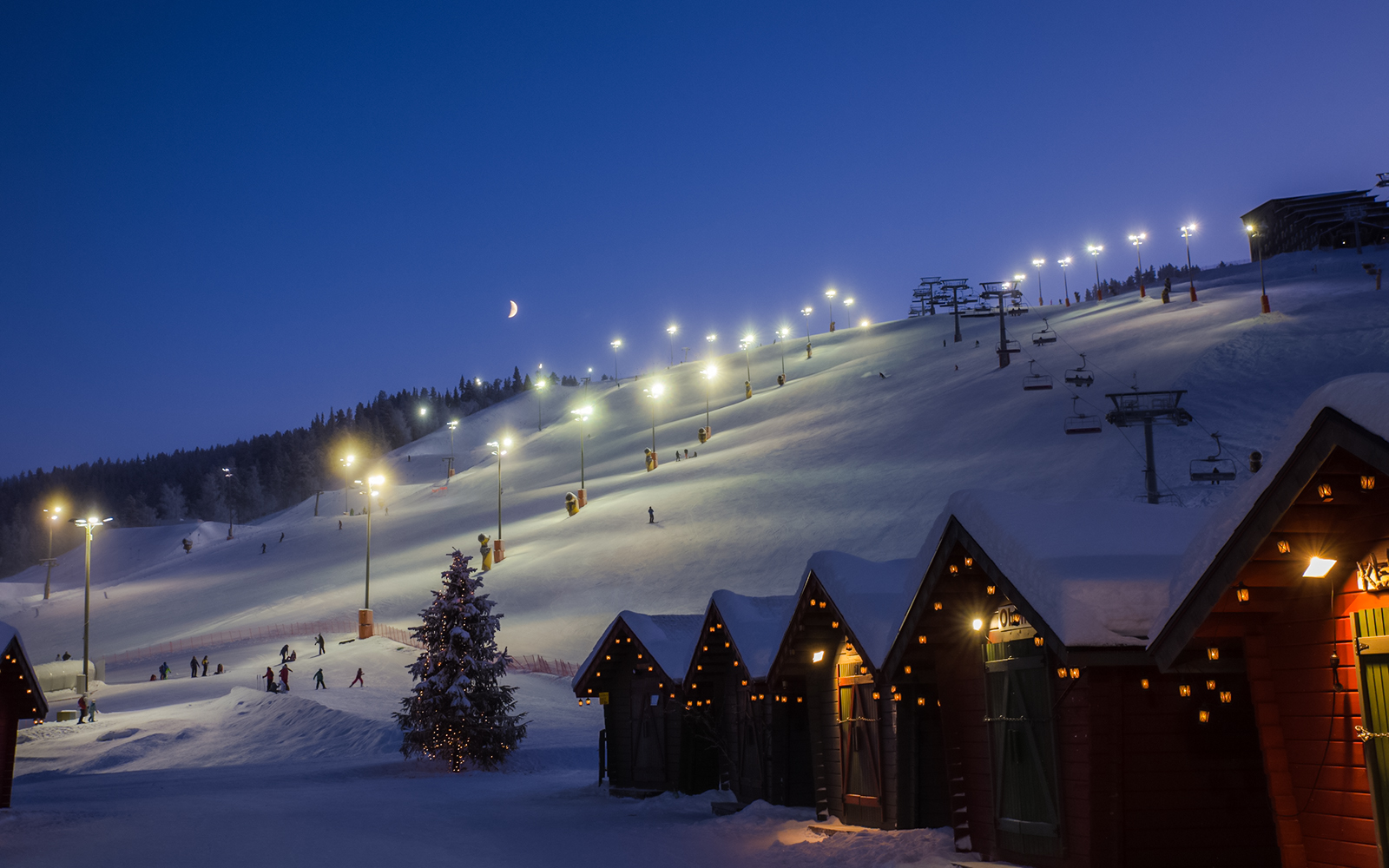 Skiers on illuminated slope with cable way in Finland at dusk.