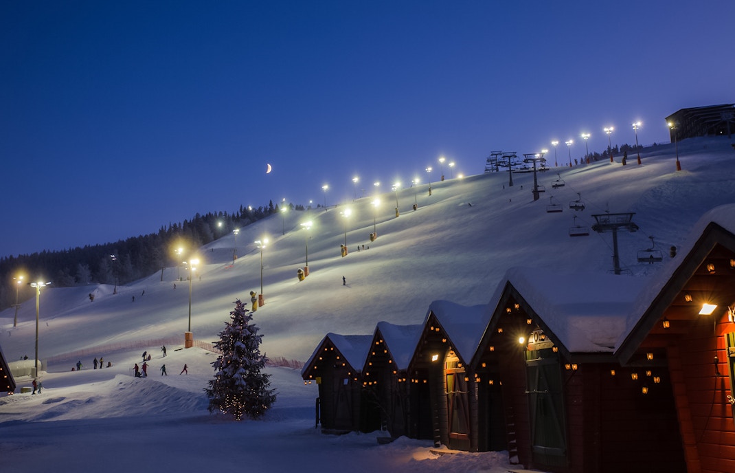 Skiers on illuminated slope with cable way in Finland at dusk.