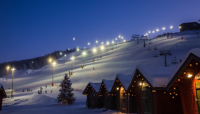 Skiers on illuminated slope with cable way in Finland at dusk.