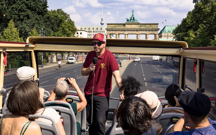 Guide speaking to tourists on Bigbus HOHO Berlin with Brandenburg Gate in view.