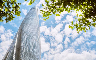 Shanghai Tower against a blue sky with clouds and green leaves.