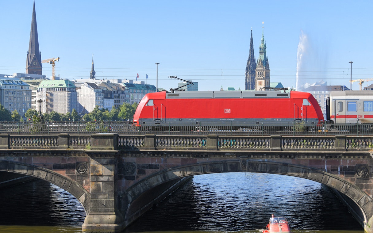 Deutsche Bahn train crossing bridge in Hamburg with city skyline in background.