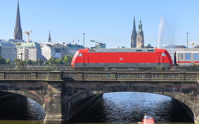 Deutsche Bahn train crossing bridge in Hamburg with city skyline in background.