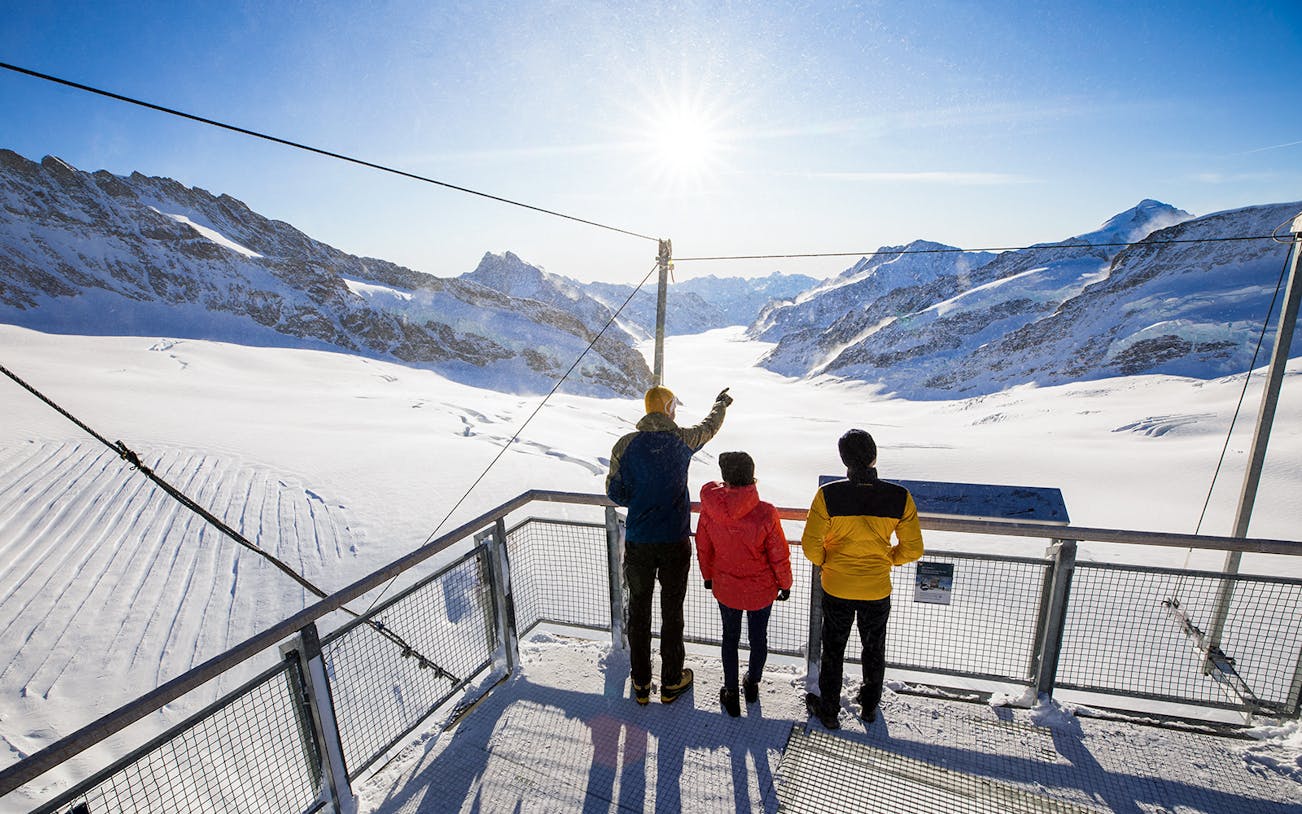 Visitors on a viewing platform overlooking snowy peaks at Jungfraujoch, Switzerland.