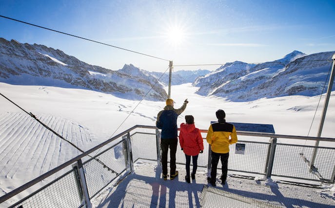 Visitors on a viewing platform overlooking snowy peaks at Jungfraujoch, Switzerland.
