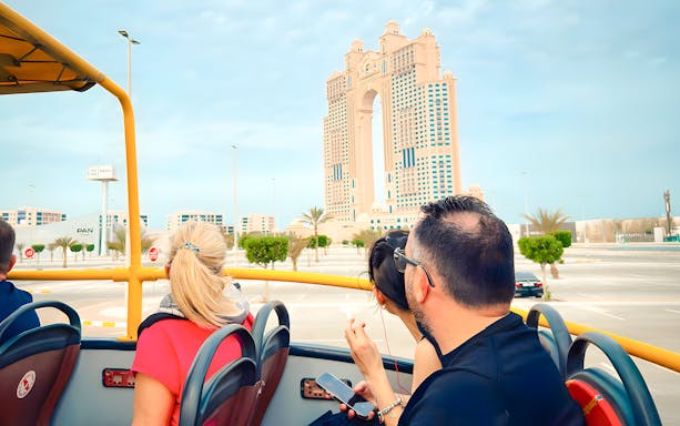 Hop on hop off bus tour near Rixos Marina Abu Dhabi with passengers viewing skyline.