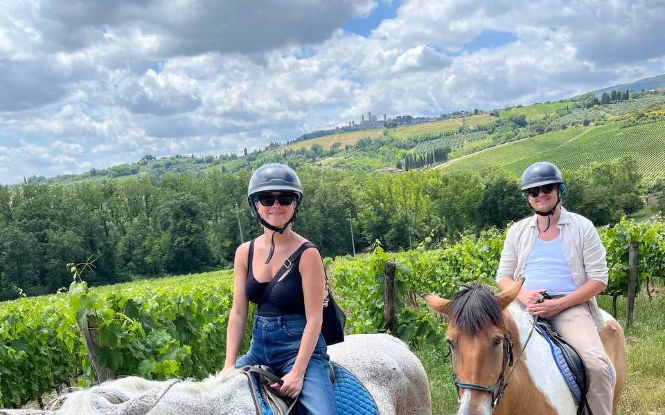 Horseback riders in Tuscany countryside with San Gimignano in the background.
