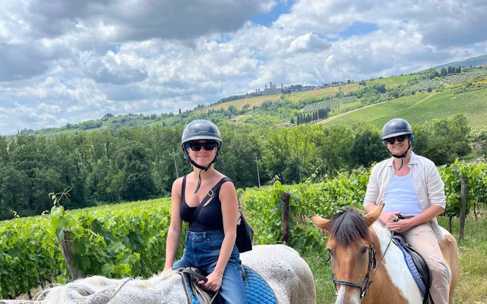 Horseback riders in Tuscany countryside with San Gimignano in the background.