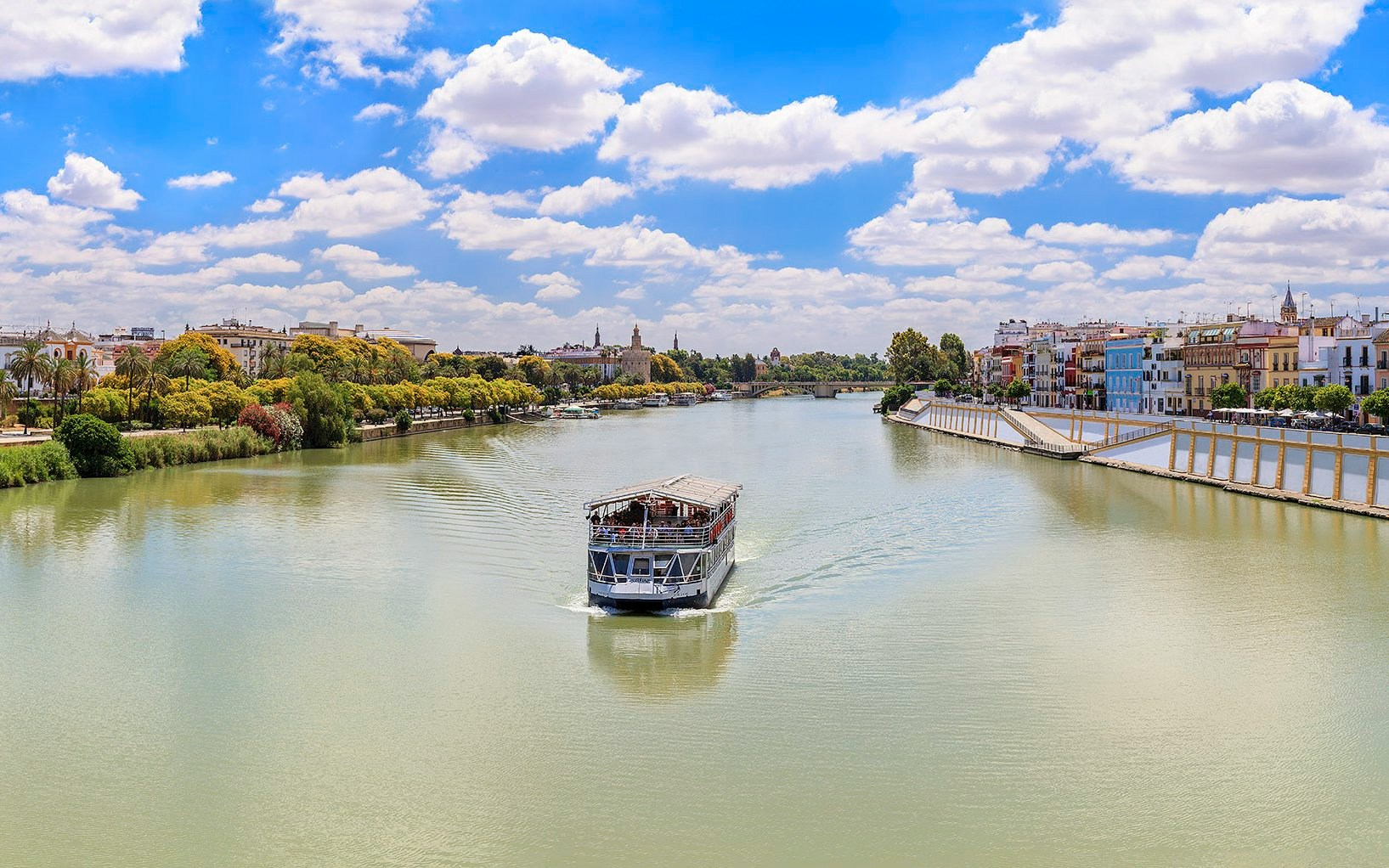 Cruise boat on Guadalquivir River with Seville skyline in the background.