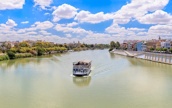 Cruise boat on Guadalquivir River with Seville skyline in the background.