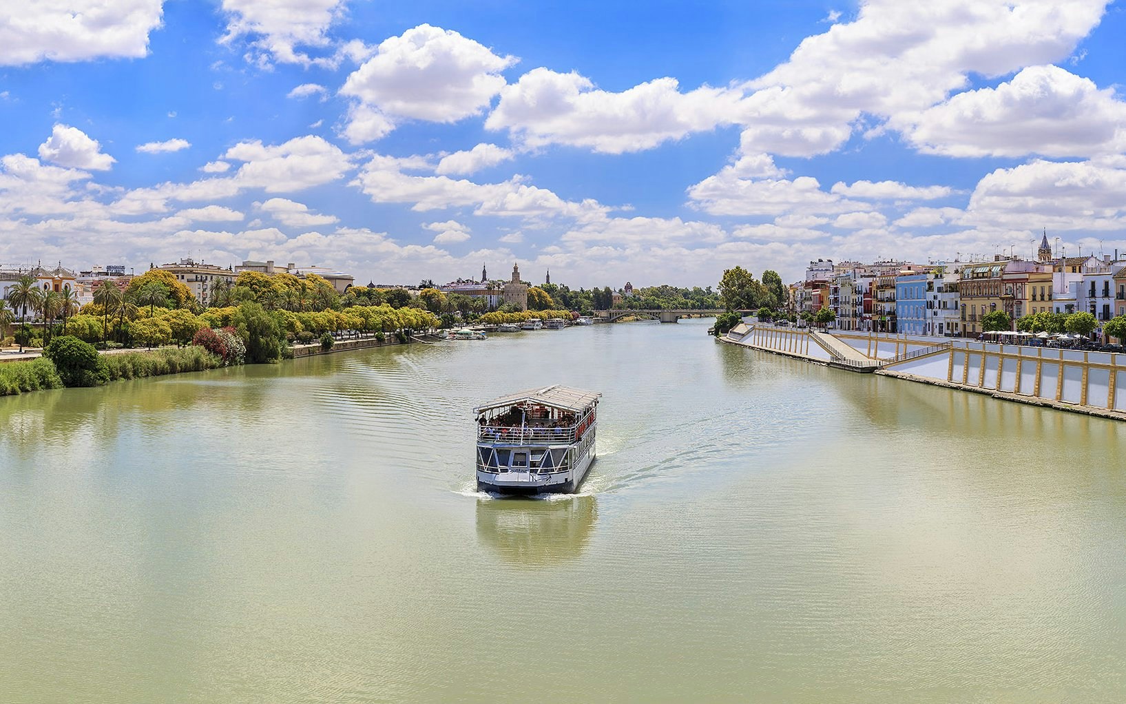 Cruise boat on Guadalquivir River with Seville skyline in the background.