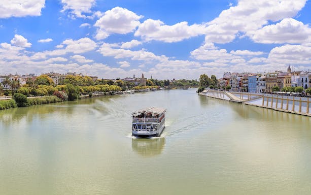 Cruise boat on Guadalquivir River with Seville skyline in the background.