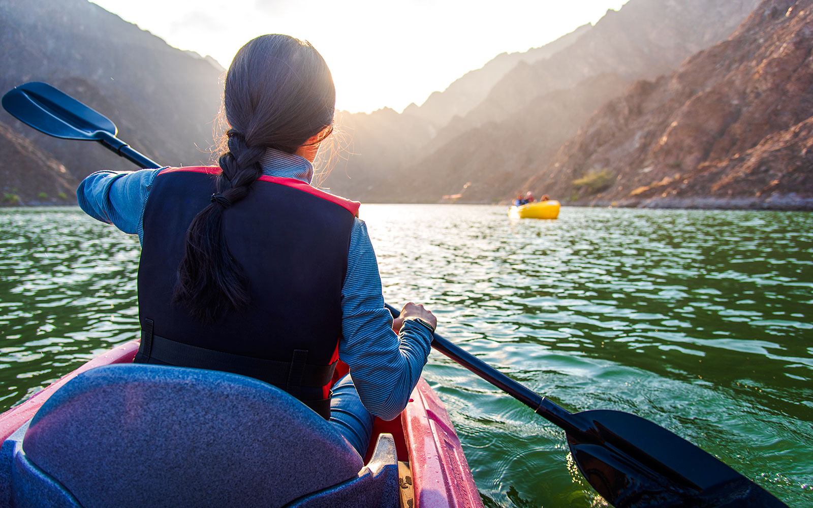 Woman kayaking on Hatta Lake with mountains in the background.