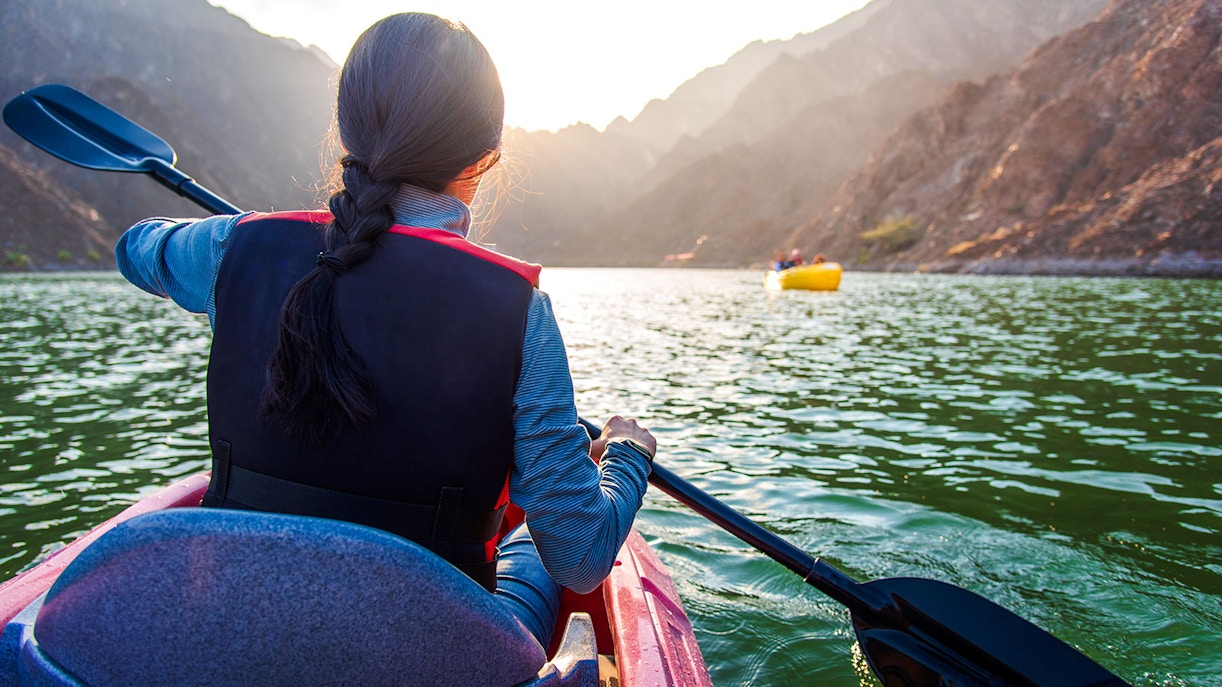 Woman kayaking on Hatta Lake with mountains in the background.