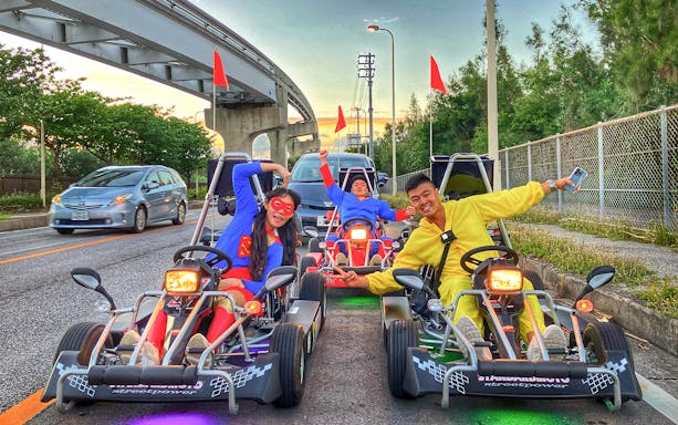 Go-karting in Okinawa with participants in colorful costumes on a city street.