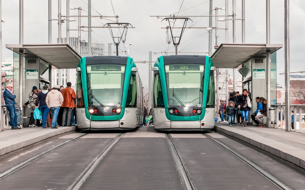 Tourists boarding trams at a Barcelona station with cityscape views.