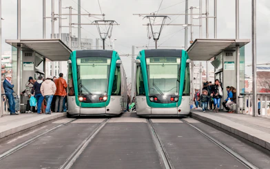 Tourists boarding trams at a Barcelona station with cityscape views.