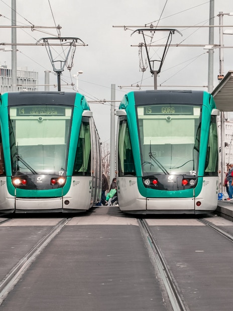 Tourists boarding trams at a Barcelona station with cityscape views.