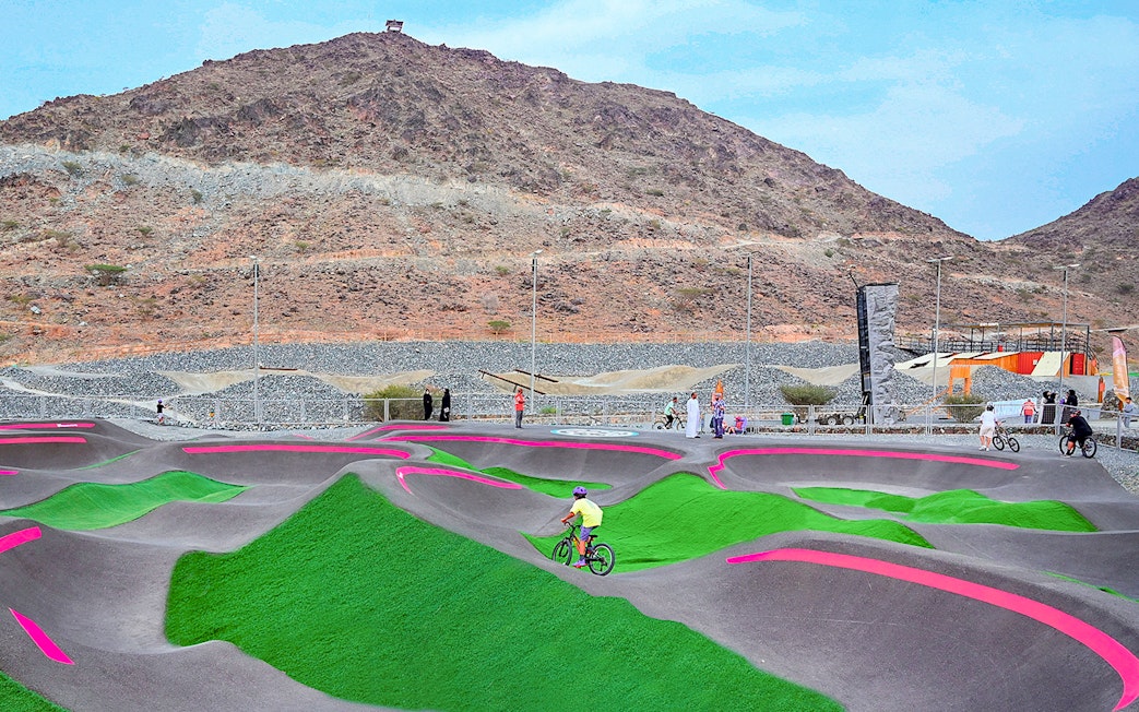 Cyclists on pump track at Fujairah Adventure Park with mountain backdrop.