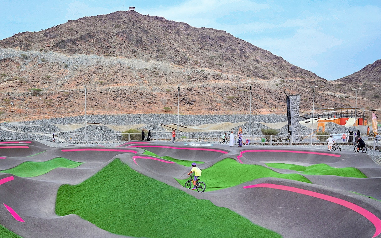 Cyclists on pump track at Fujairah Adventure Park with mountain backdrop.