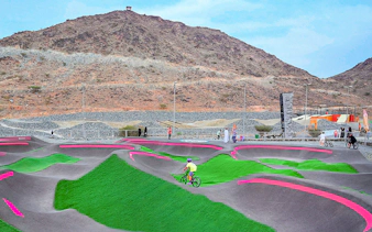 Cyclists on pump track at Fujairah Adventure Park with mountain backdrop.