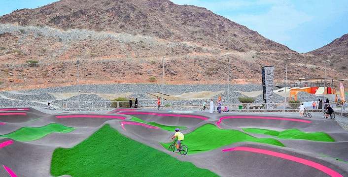 Cyclists on pump track at Fujairah Adventure Park with mountain backdrop.