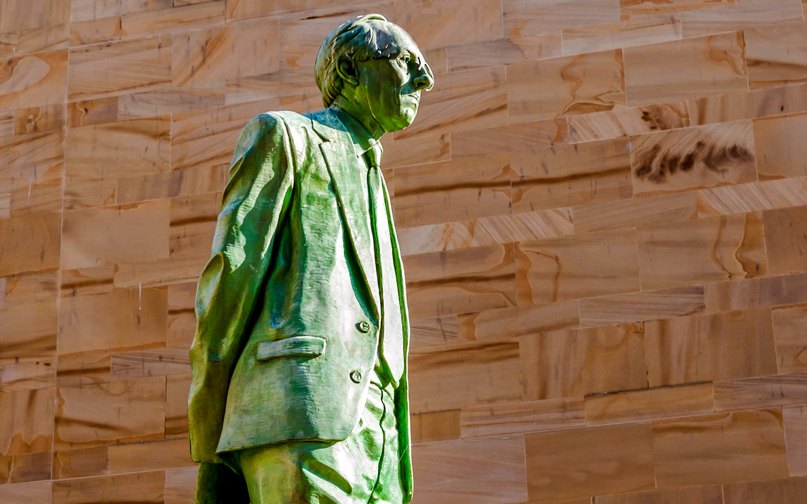 Donald Dewar statue in Glasgow against a stone wall background.
