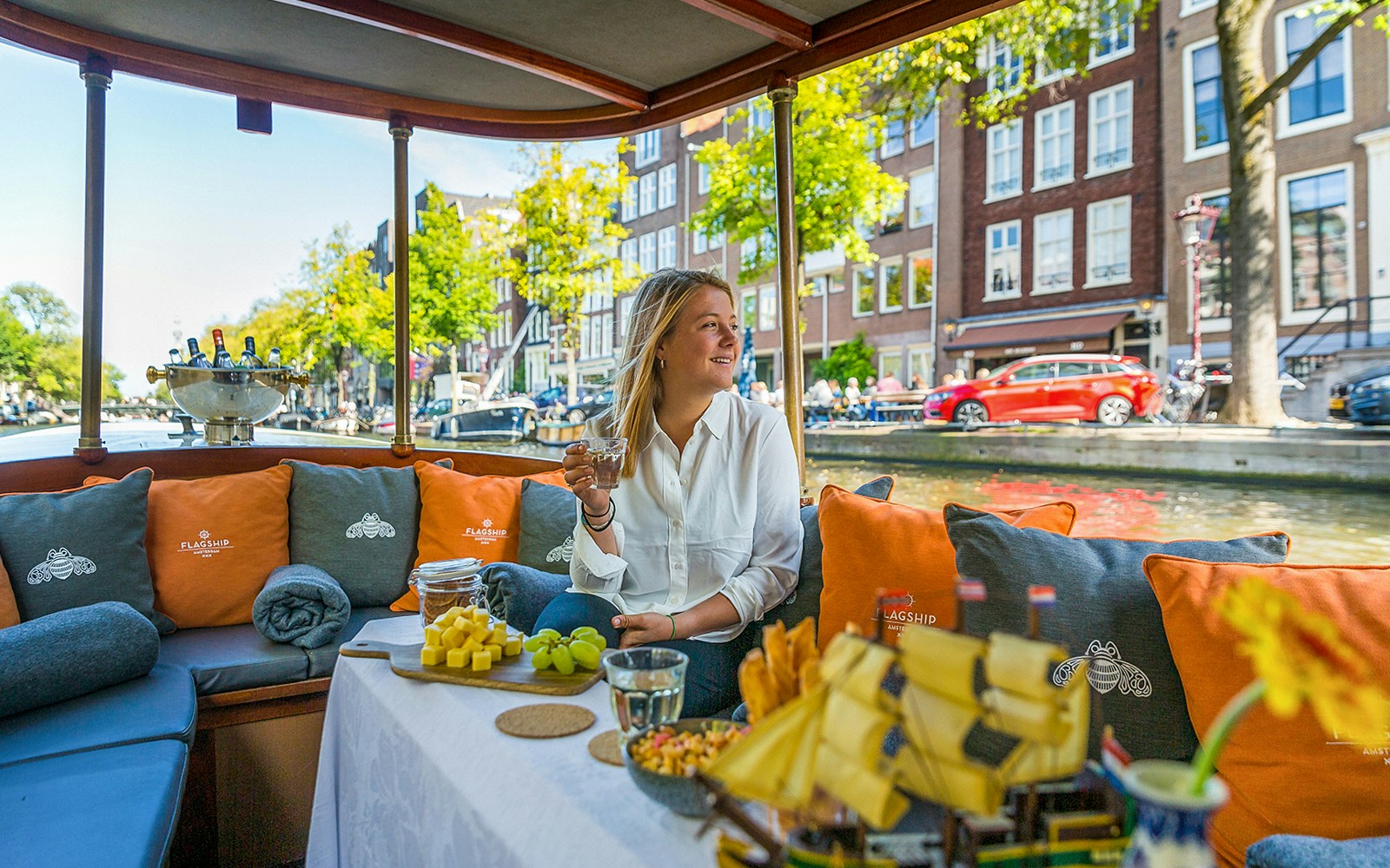 Amsterdam canal cruise with passengers enjoying drinks on an open boat.