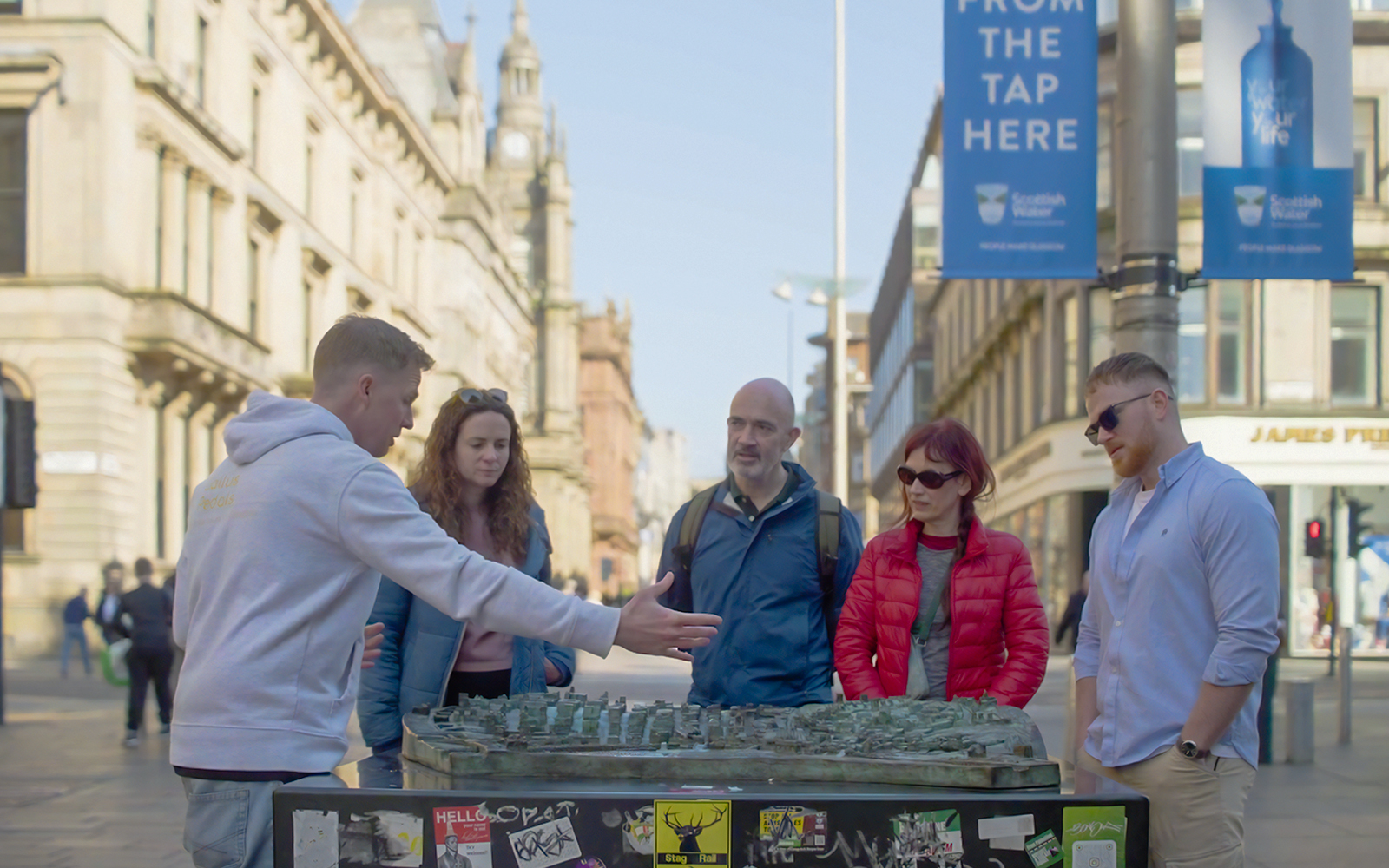 Tour guide explaining a city model to a group during a walking tour in Glasgow.