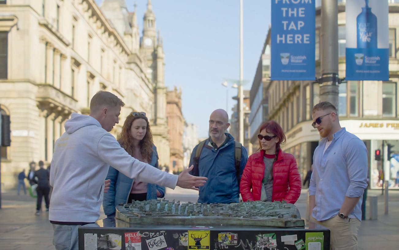 Tour guide explaining a city model to a group during a walking tour in Glasgow.