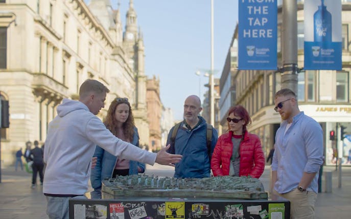 Tour guide explaining a city model to a group during a walking tour in Glasgow.