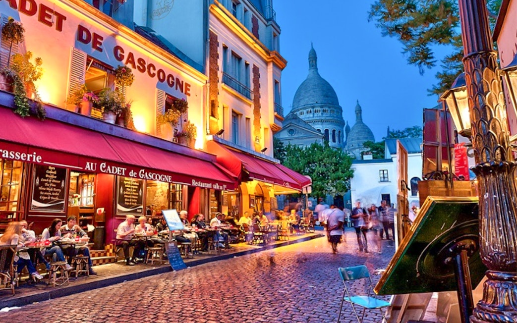 Café scene in Montmartre with Sacré-Cœur in the background during evening.