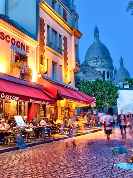 Café scene in Montmartre with Sacré-Cœur in the background during evening.