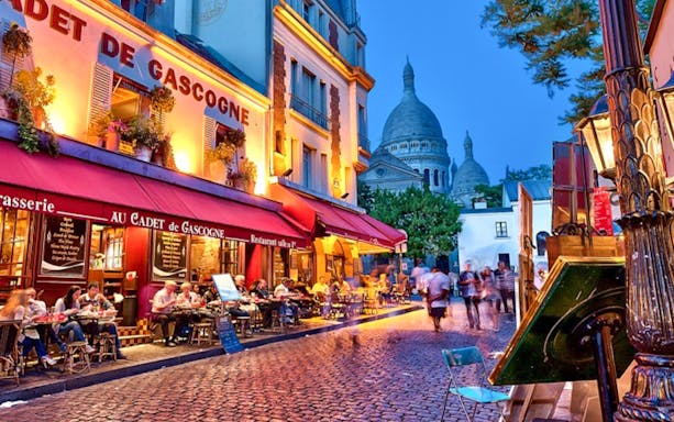 Café scene in Montmartre with Sacré-Cœur in the background during evening.