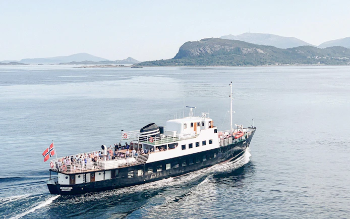 Fjord boat cruising near Ålesund with passengers on deck.