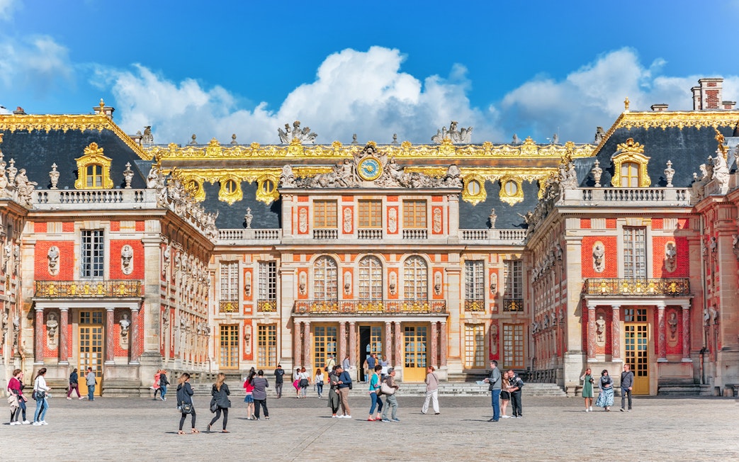 Visitors walking in front of the ornate facade of the Palace of Versailles, France.