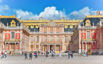 Visitors walking in front of the ornate facade of the Palace of Versailles, France.