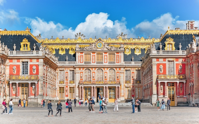 Visitors walking in front of the ornate facade of the Palace of Versailles, France.