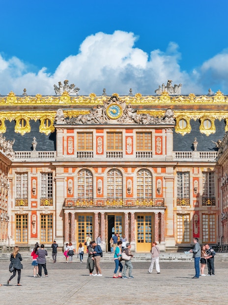 Visitors walking in front of the ornate facade of the Palace of Versailles, France.