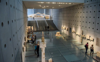 Visitors exploring ancient artifacts inside Acropolis Museum, Athens.