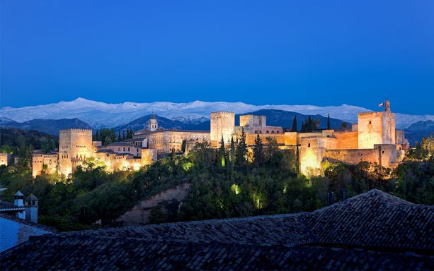 Alhambra illuminated at night with Sierra Nevada backdrop, Granada, Spain.