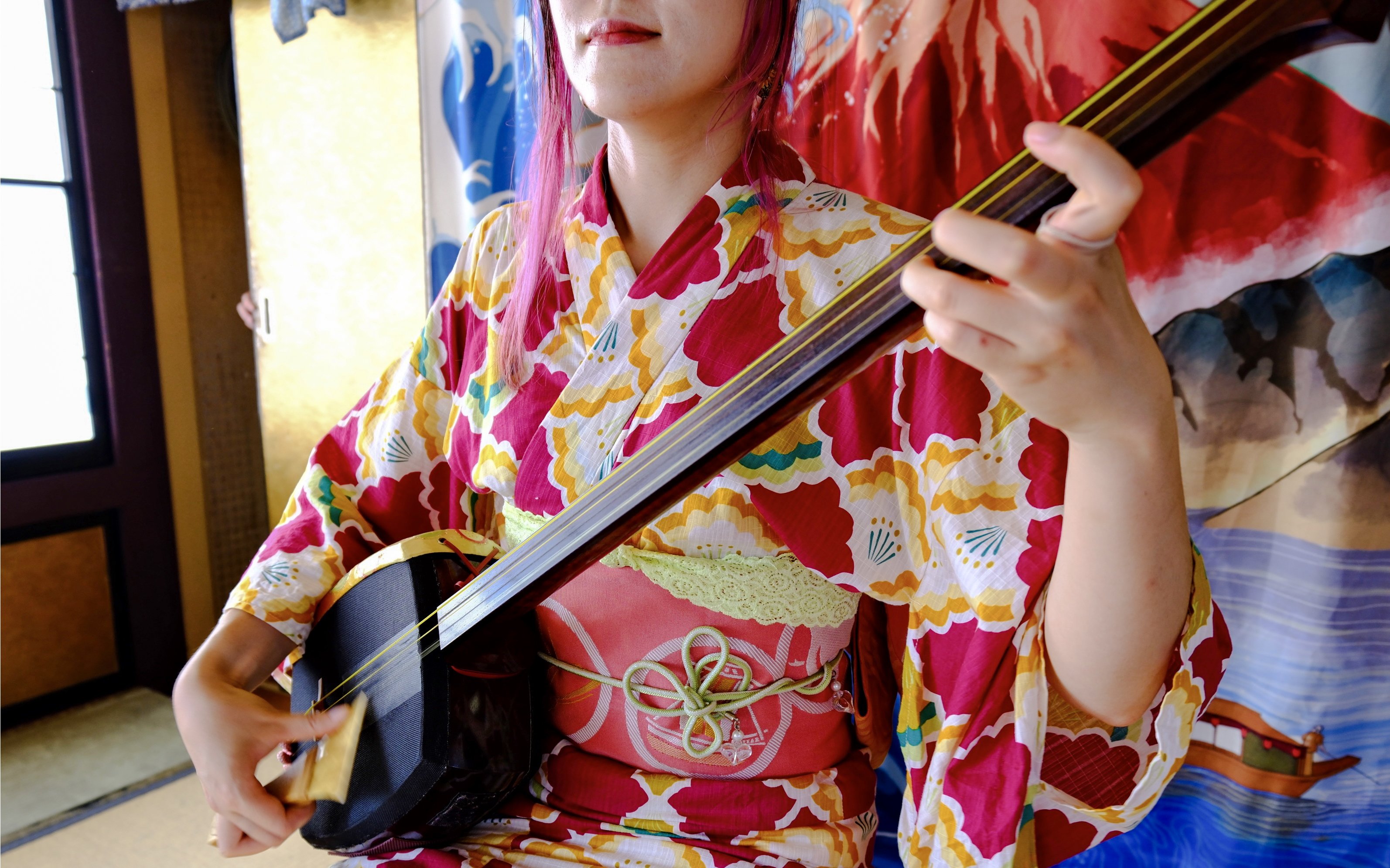 Person in colorful kimono playing shamisen during Tokyo Spring Tea Ceremony.