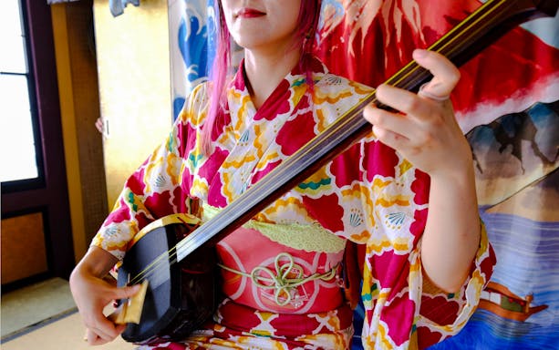 Person in colorful kimono playing shamisen during Tokyo Spring Tea Ceremony.