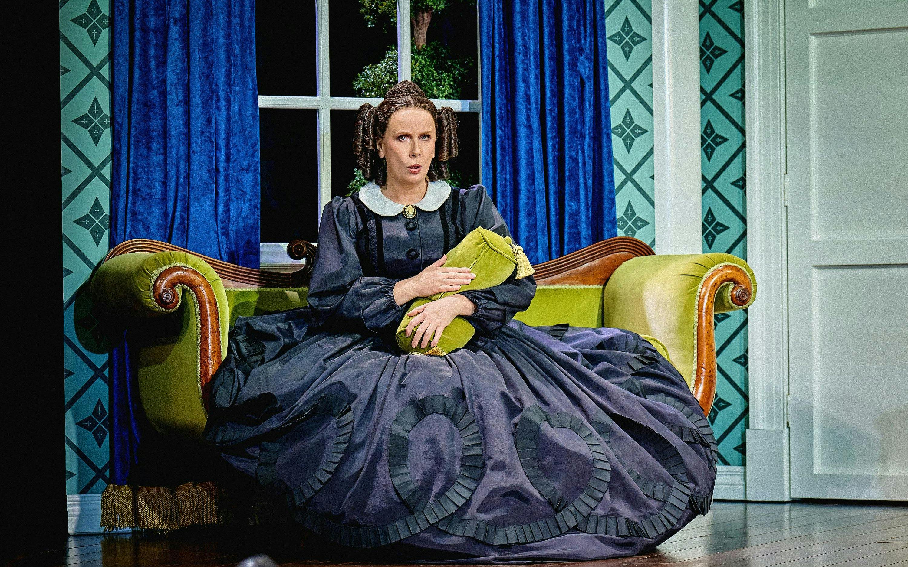 Stage scene from Oh, Mary Westend show with actor in period costume on a vintage sofa.
