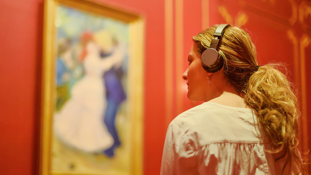 Visitor with headphones viewing French Impressionist painting at NGV Melbourne exhibition.