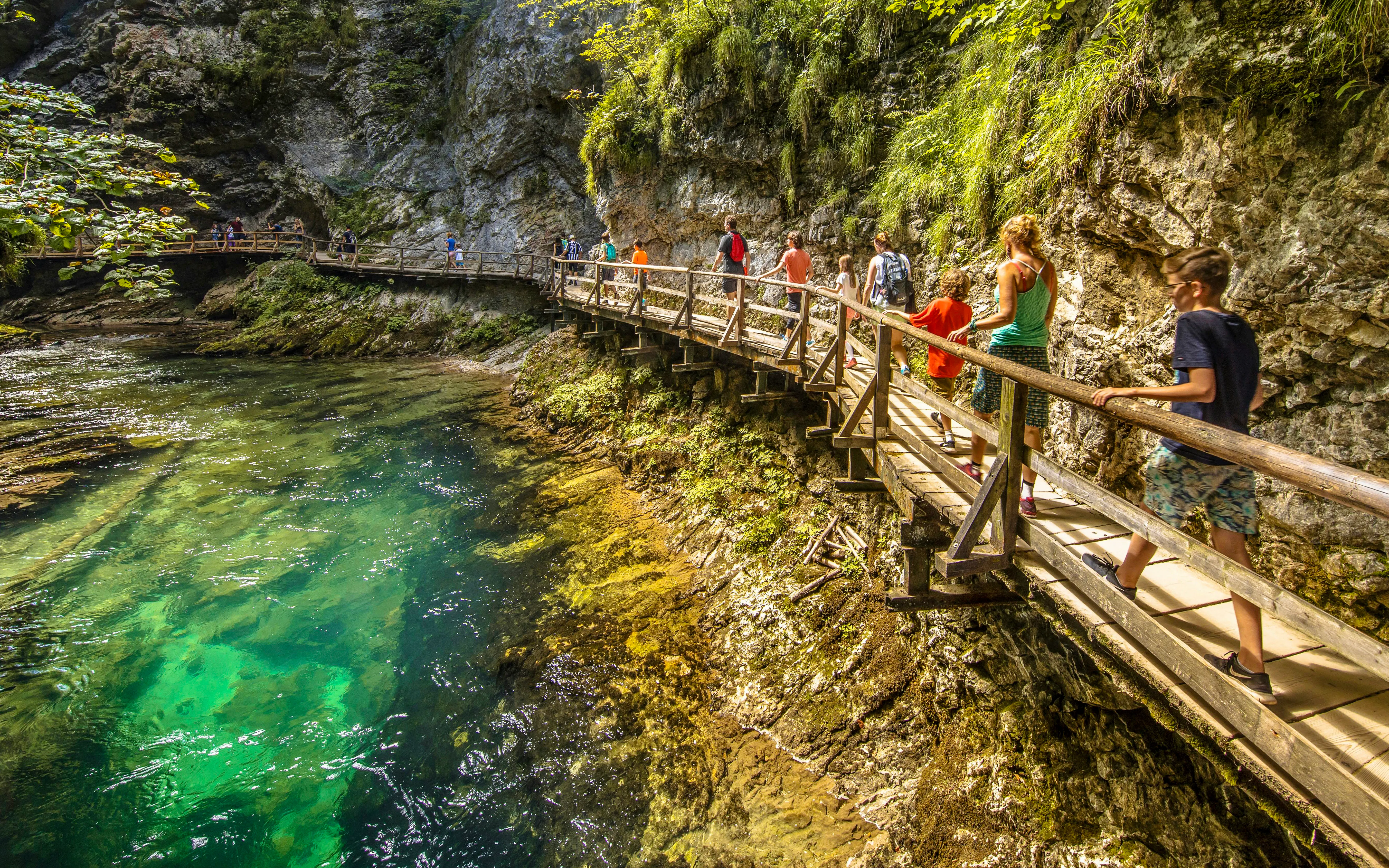 Visitors walking on the boardwalk at Vintgar Gorge, Slovenia, with clear water below.